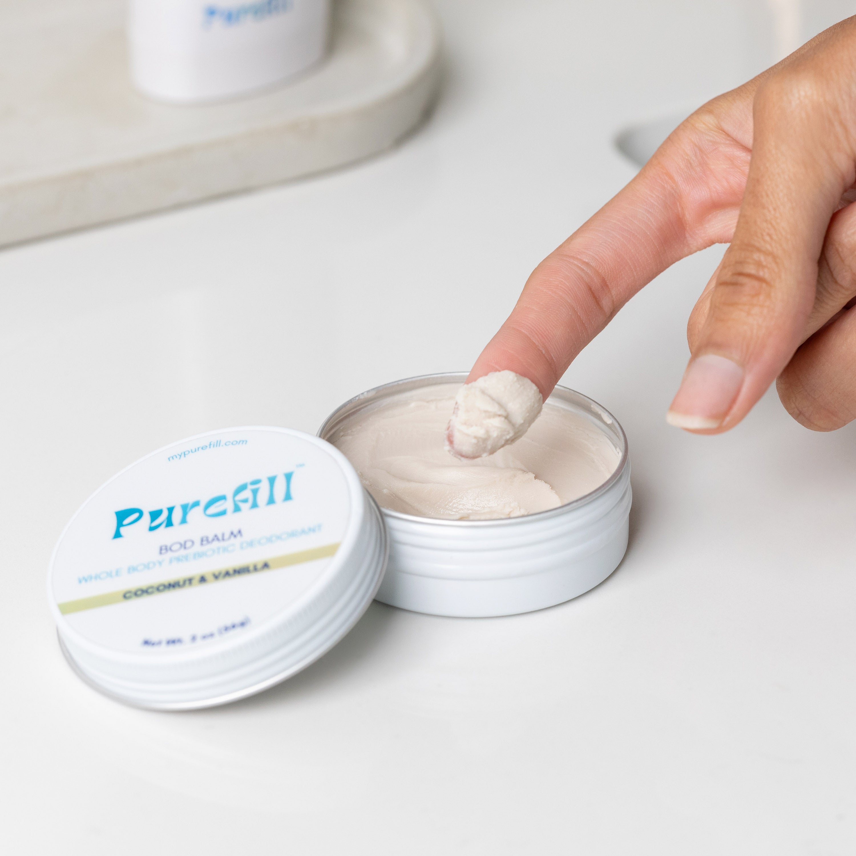 Hand applying Purefill bod balm on a white surface.