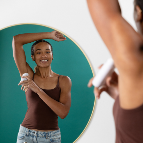 Young lady looking in the mirror at her reflection applying Purefill Deodorant and smiling.